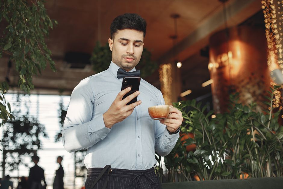 A young man in a stylish cafe checks his smartphone while enjoying a coffee.